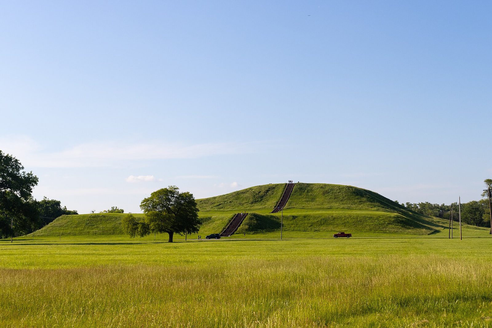 Monks Mound at Cahokia Mounds, a broad grassy earthen platform mound with stairs climbing its face under a blue summer sky